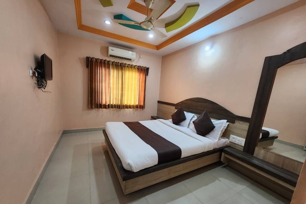 Une chambre à coucher comprenant un lit, un ventilateur de plafond, un appareil de climatisation, un miroir et une fenêtre avec des rideaux.
