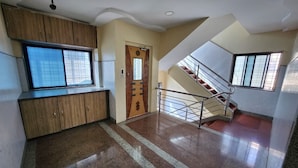 Un couloir avec une armoire en bois, une porte ornée d’un motif géométrique et un escalier avec des rampes en métal.