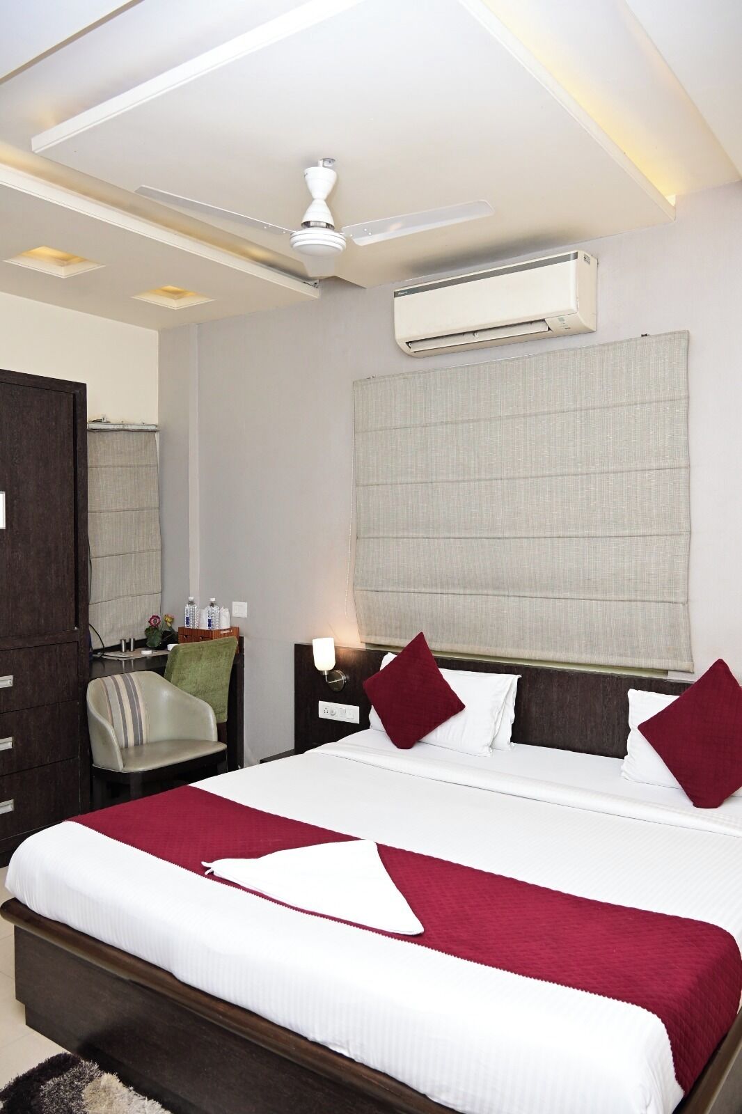 Una habitación de hotel con cama, escritorio, silla, aire acondicionado y ventilador de techo.