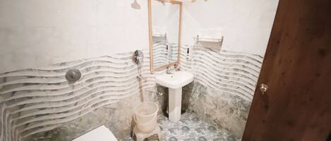 A bathroom with a marble floor, a white sink, a toilet, and a wooden door.