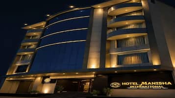 Un hôtel à plusieurs étages, doté d’une façade incurvée, de fenêtres illuminées et d’une enseigne indiquant qu’il s’agit de l’hôtel Manisha International.