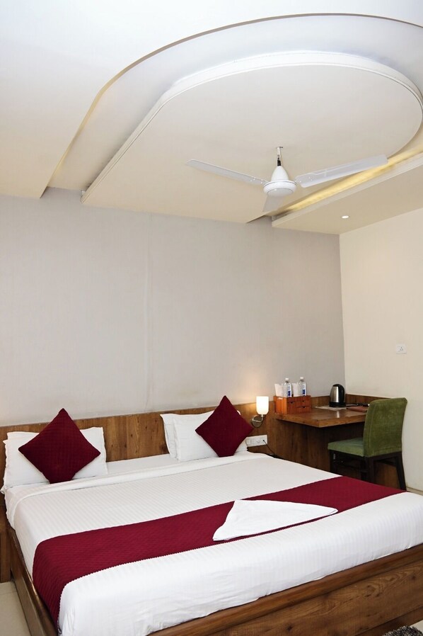 A hotel room with a bed, a desk, a chair, a ceiling fan, and a wall-mounted light.
