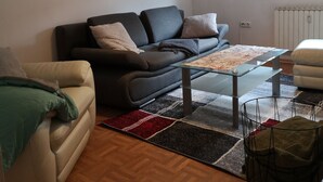 Een woonkamer met een bank, een bijzettafeltje en een kamerkleed met een patroon.