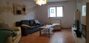A living room with a sofa, a coffee table, a television, and a window with blinds. - Vacation apartment Merkershausen  (Bad Königshofen im Grabfeld)