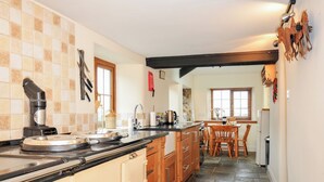 A kitchen with a stove, sink, and wooden cabinets. There is a dining area with a table and chairs. - Little Blagdon (Holsworthy)