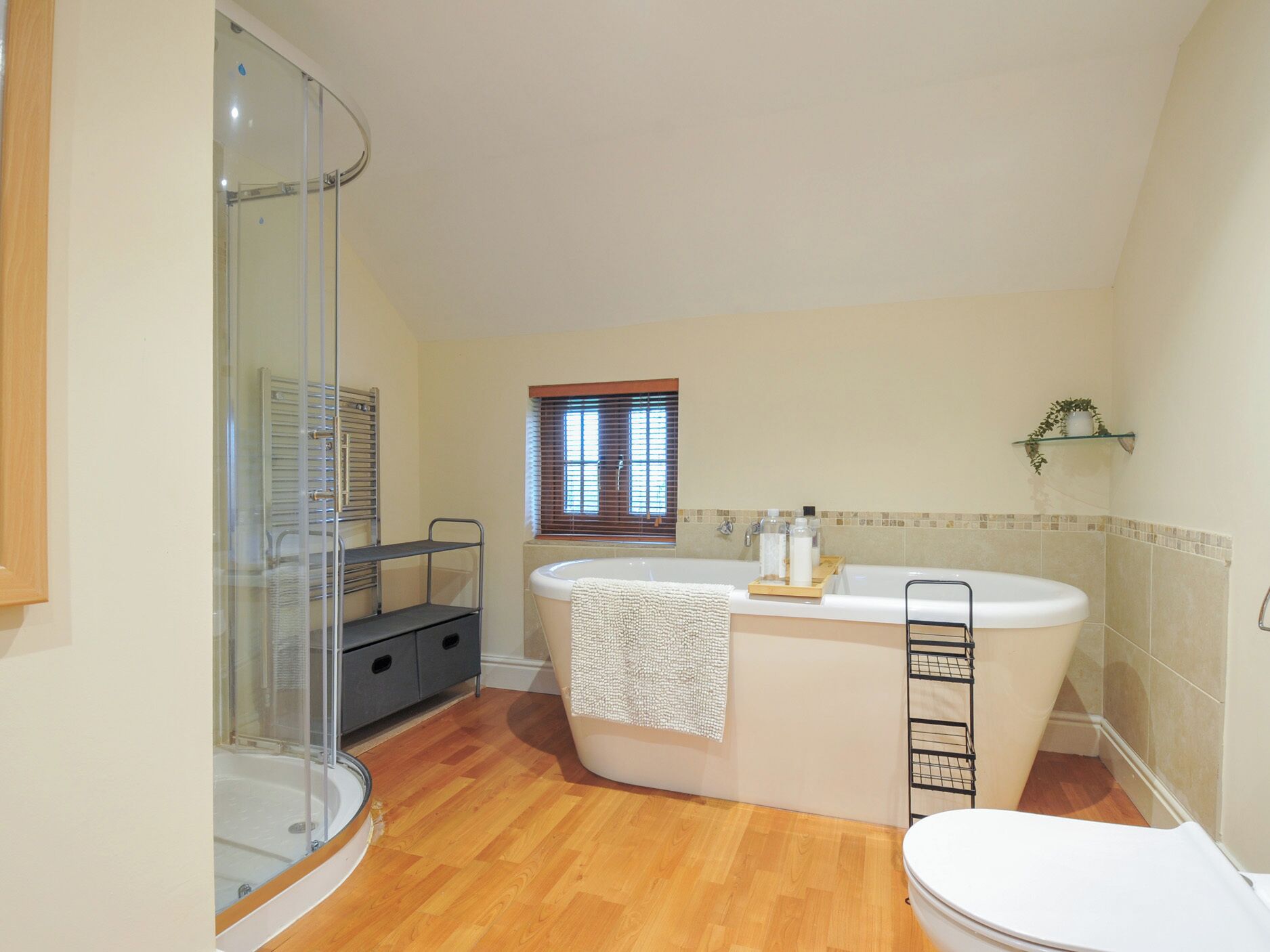 Une salle de bain avec une douche à parois de verre, une baignoire, des toilettes et une fenêtre avec des stores.