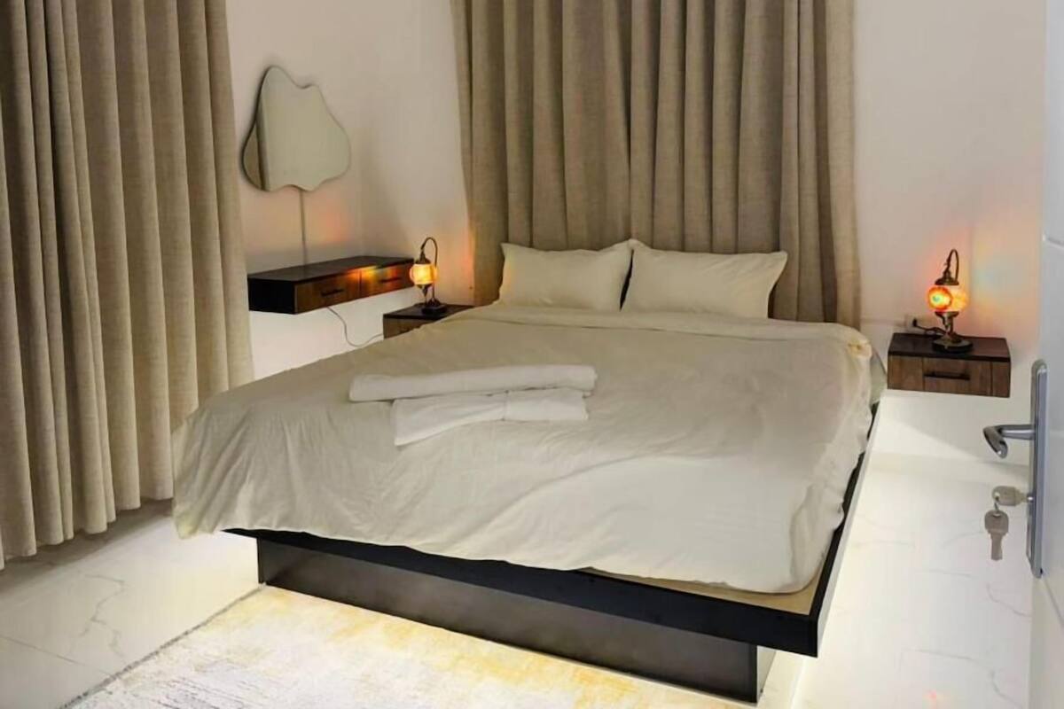 A modern bedroom with a large bed, beige curtains, and bedside lamps.