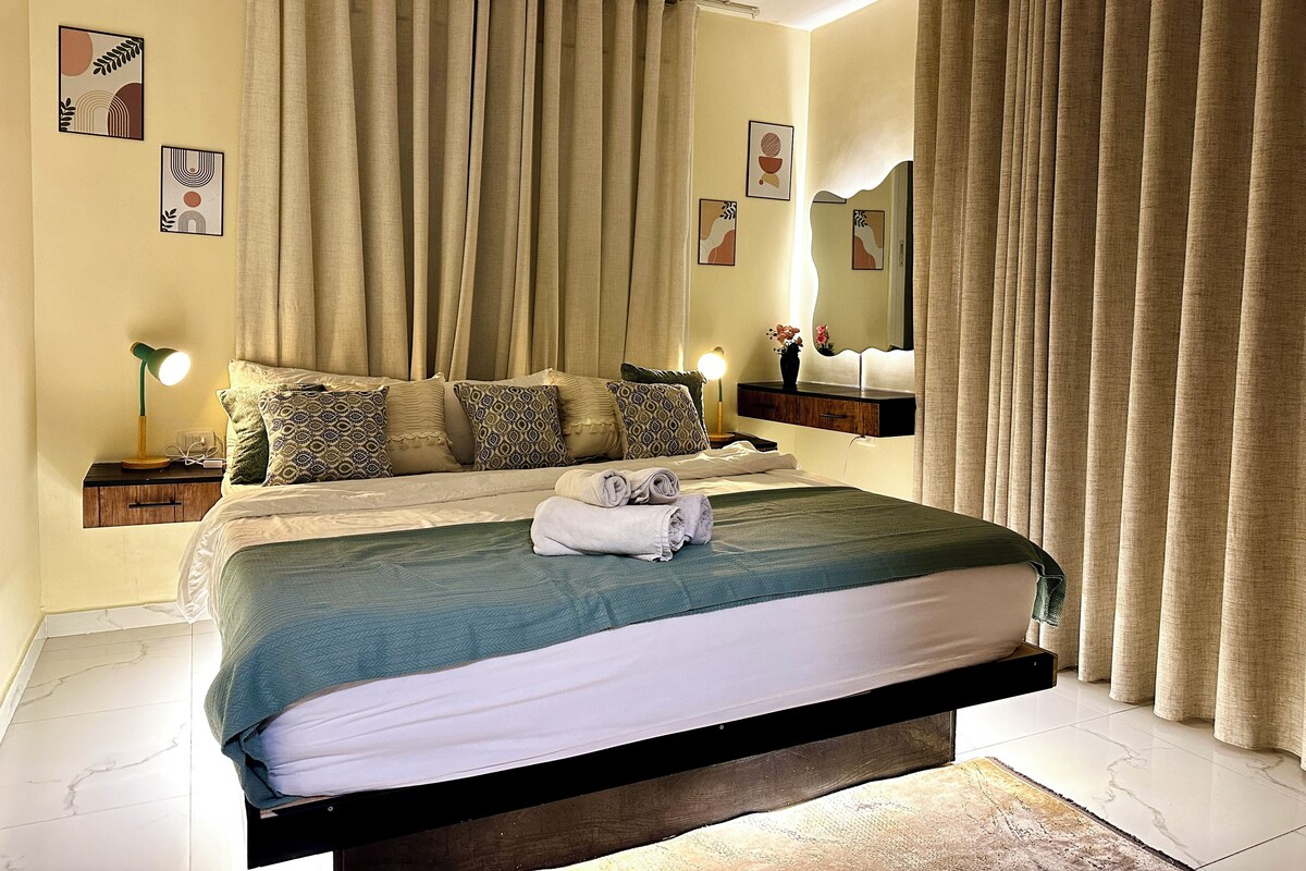 A neatly made bed with a green and white bedspread, a bedside lamp, and a nightstand with a lamp.