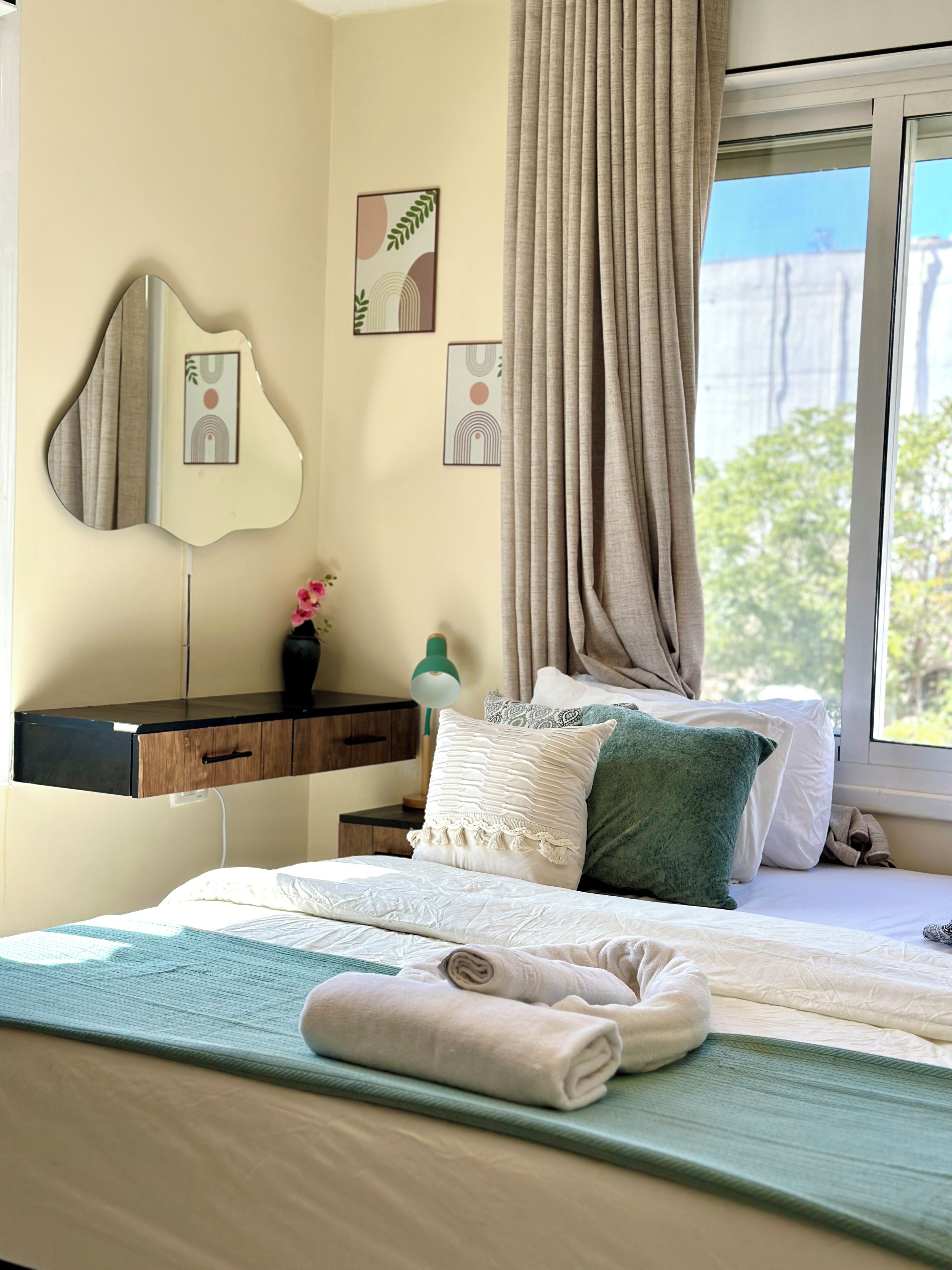 A neatly made bed with pillows, a bedside table with a lamp, a mirror, and artwork on the wall.