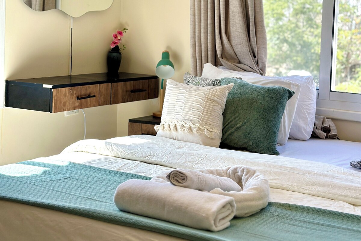 A neatly made bed with pillows, a bedside table with a lamp, a mirror, and artwork on the wall.