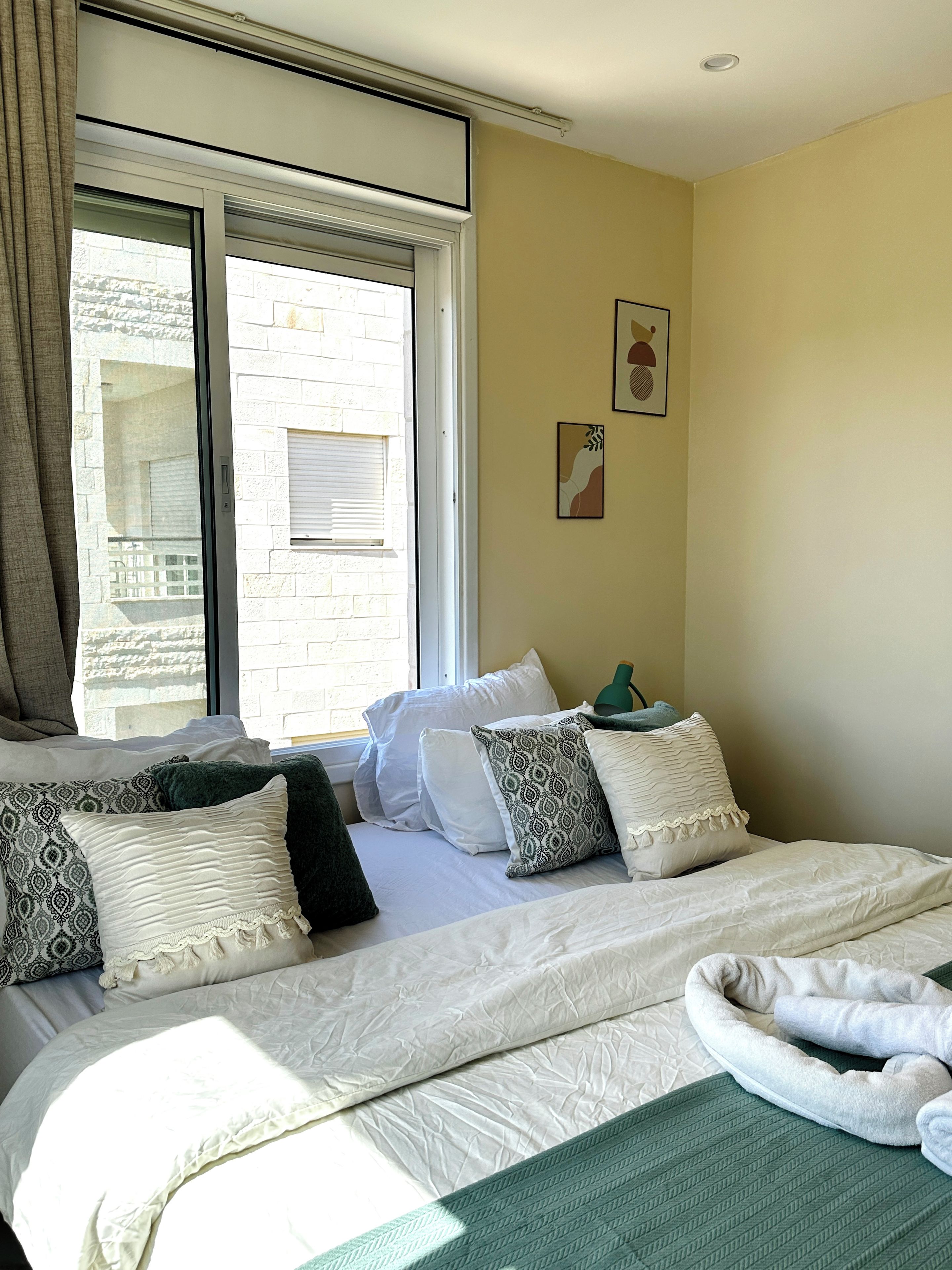 Ein Schlafzimmer mit einem Bett, Kissen, einer grünen Decke und einem Fenster mit Jalousien.