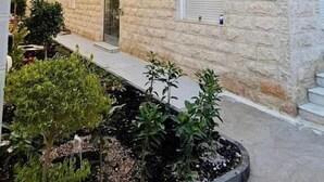 A stone building with multiple windows and a door, surrounded by a small garden area with various plants. - Beit Ahlan Suites (Amman)