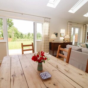A dining area with a wooden table, a vase of red flowers, and a blue and white plate. - Beautiful Barn, Stunning Views, Parking & Garden (Gloucestershire)