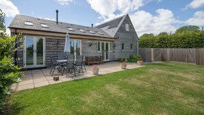 Een houten huis met een terras, een overdekte zithoek en een omheinde achtertuin.