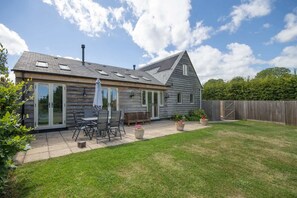 A wooden house with a patio, a covered seating area, and a fenced backyard. - Beautiful Barn, Stunning Views, Parking & Garden (Gloucestershire)