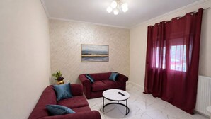 Een woonkamer met twee rode banken, een witte salontafel, een schilderij aan de muur en een raam met rode gordijnen.