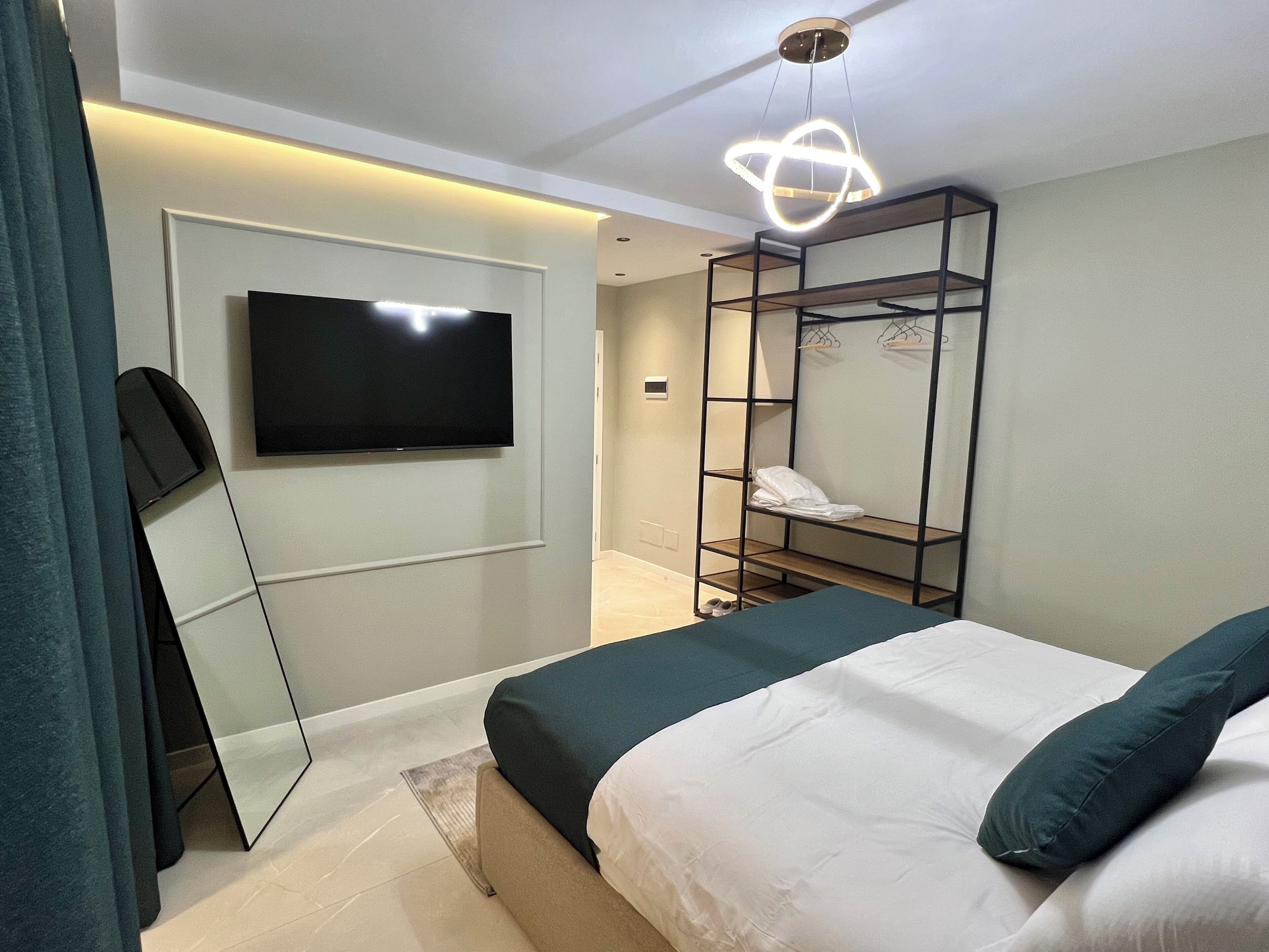 A modern hotel room with a bed, a TV mounted on the wall, a mirror, and a built-in wardrobe.
