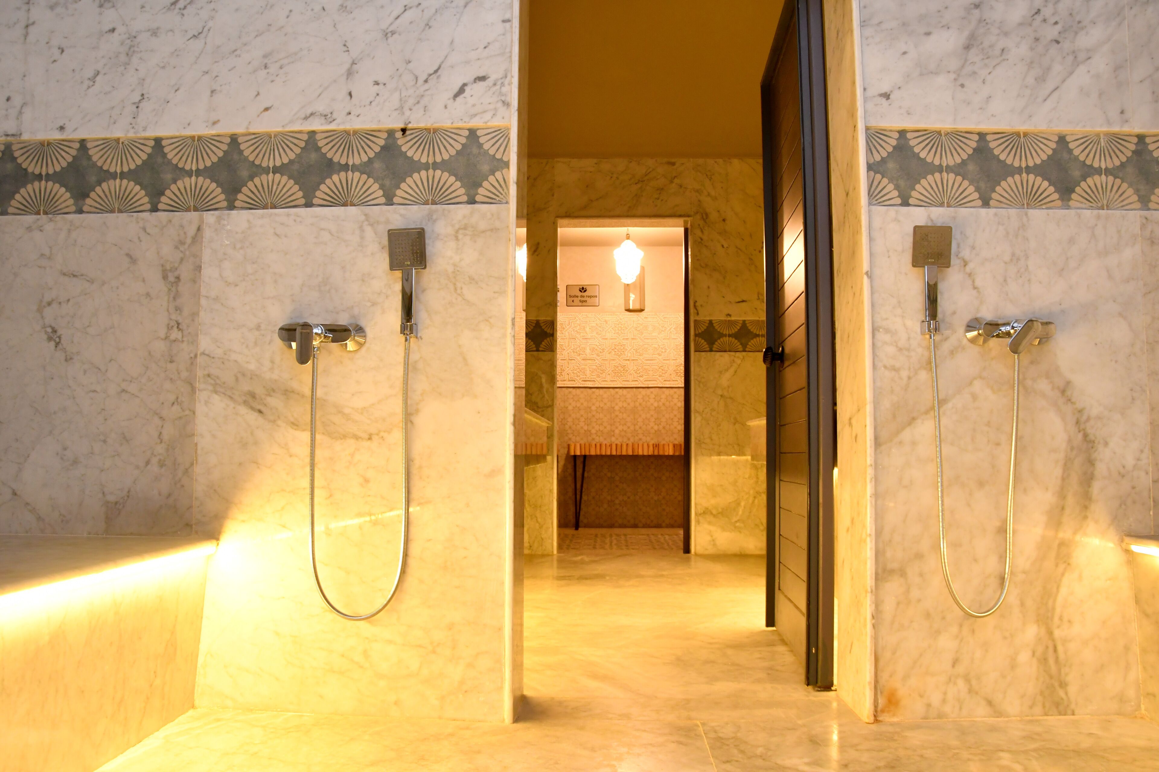 A marble bathroom with two showerheads, a towel rack, and a light fixture.