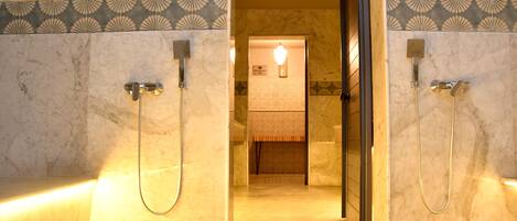 A marble bathroom with two showerheads, a towel rack, and a light fixture.
