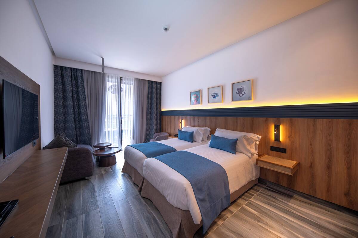 A hotel room with two beds, a desk, a TV, and a wooden wall panel.