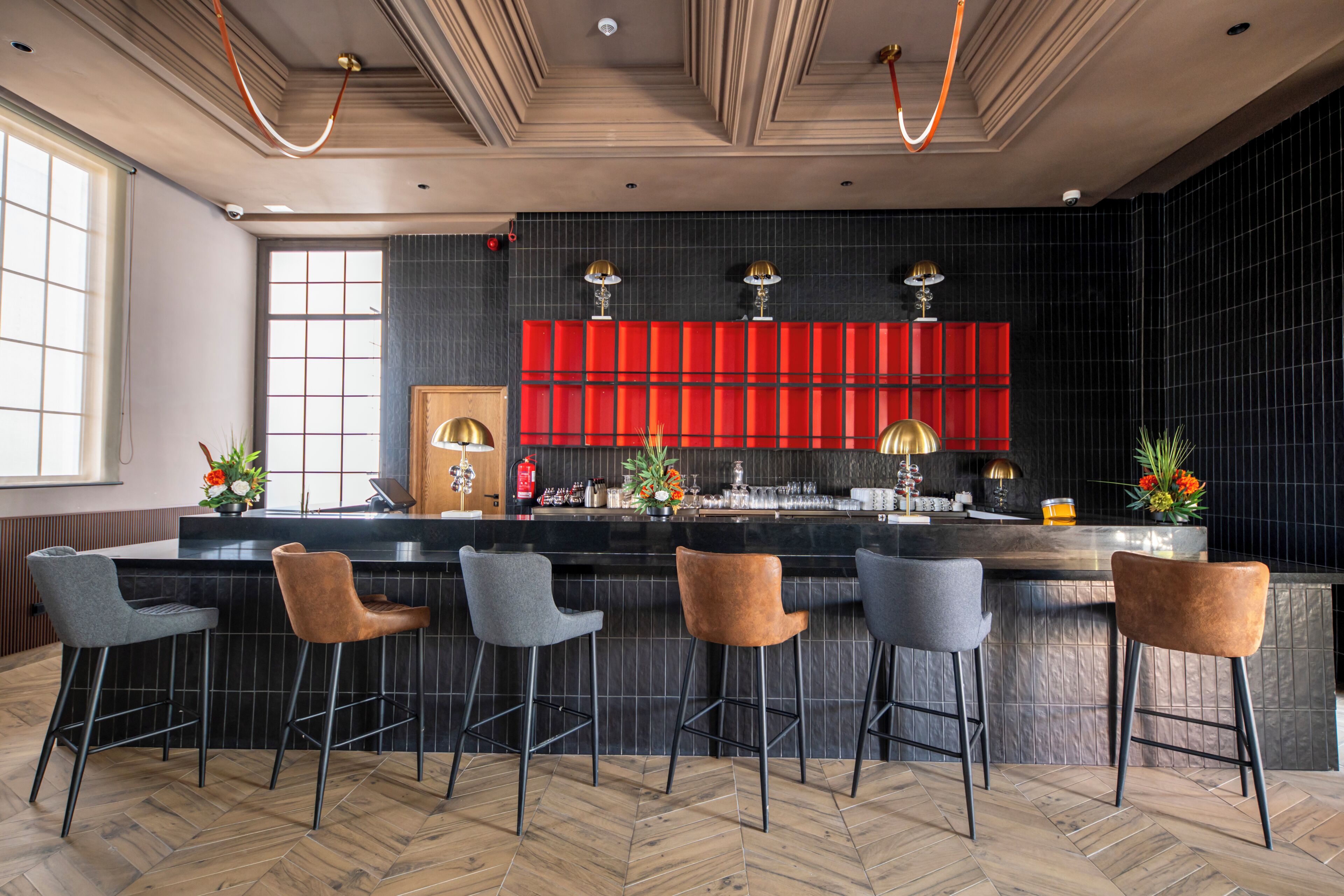 A bar area with a black countertop, four bar stools, and a red shelf with decorative items.