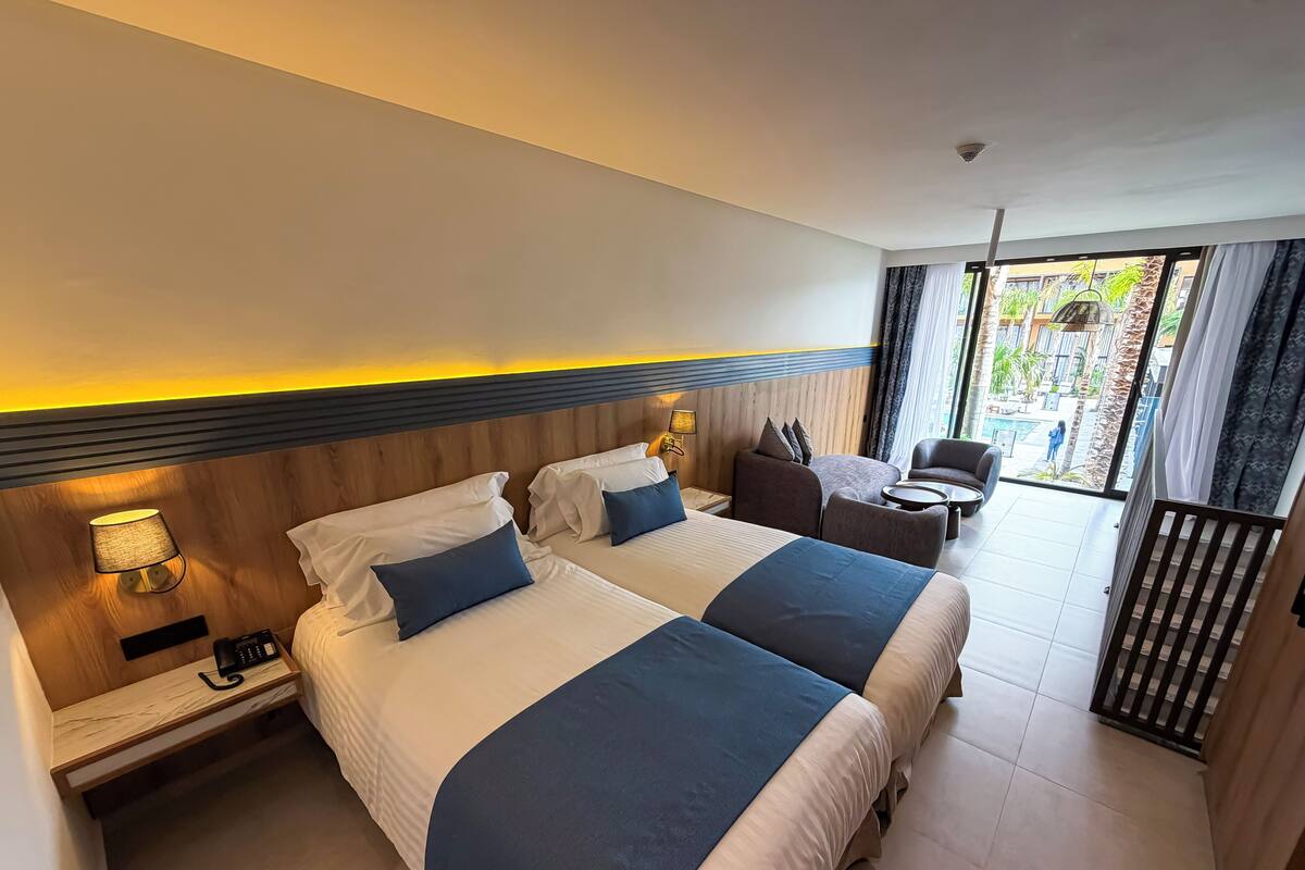 A hotel room with two beds, a desk, a chair, and a view of the outdoor area.