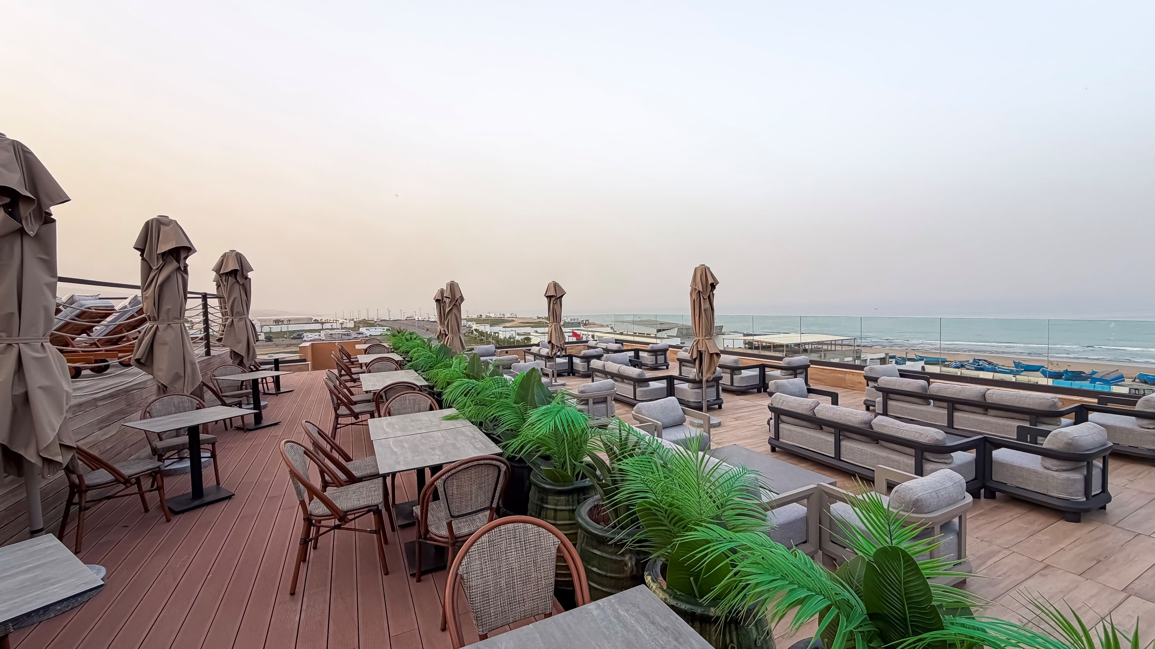 A rooftop terrace with outdoor seating, potted plants, and a view of the beach and ocean.