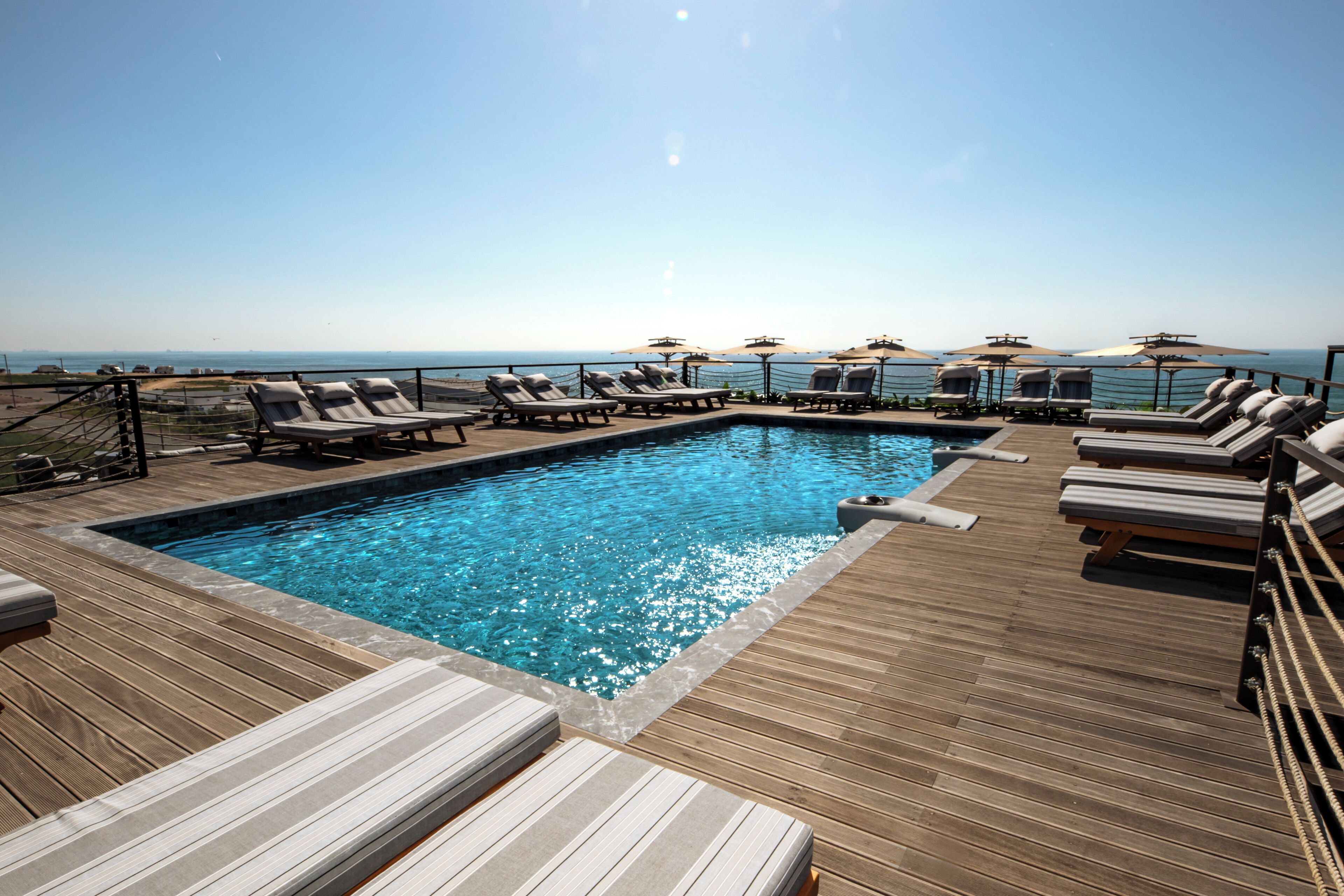 A poolside area with lounge chairs and umbrellas, overlooking a clear blue sky and ocean.