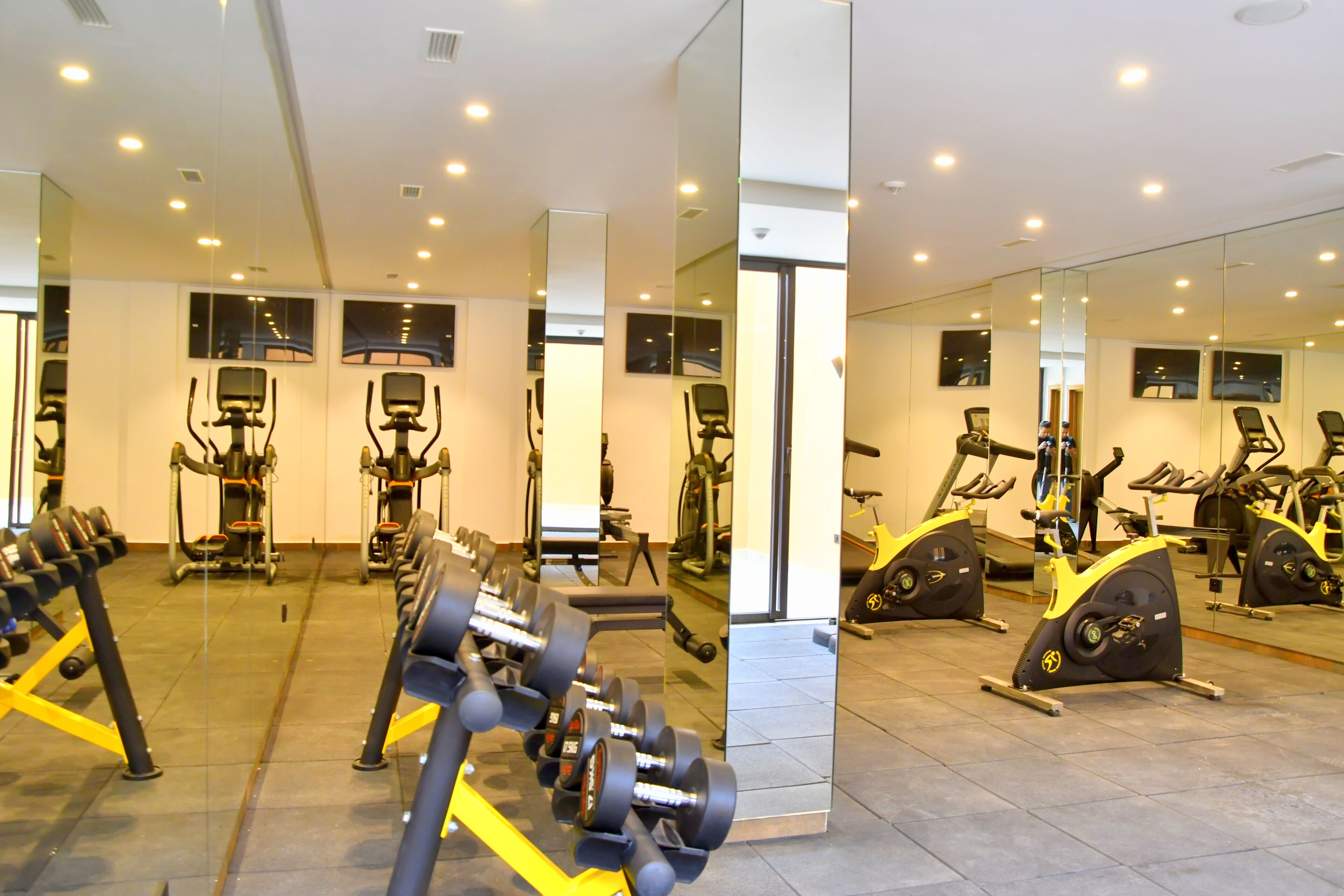 A gym with exercise equipment, mirrors, and a tiled floor.
