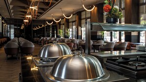 A modern restaurant interior with a long counter, metal food covers, and a potted plant on the bar. - Palm Taghazout Hotel (Tamraght)