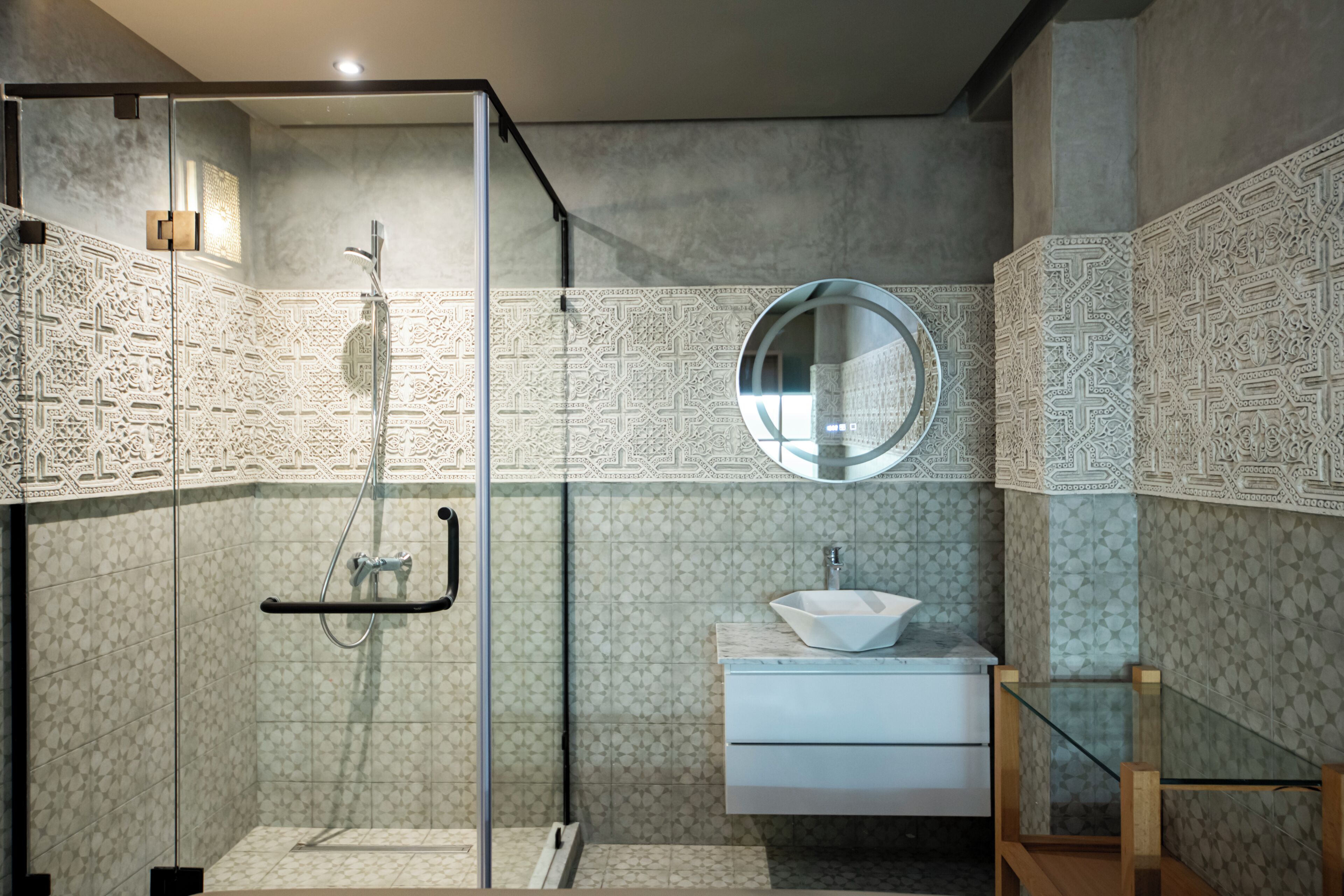 A modern bathroom with a glass shower enclosure, a round mirror, and a white sink.