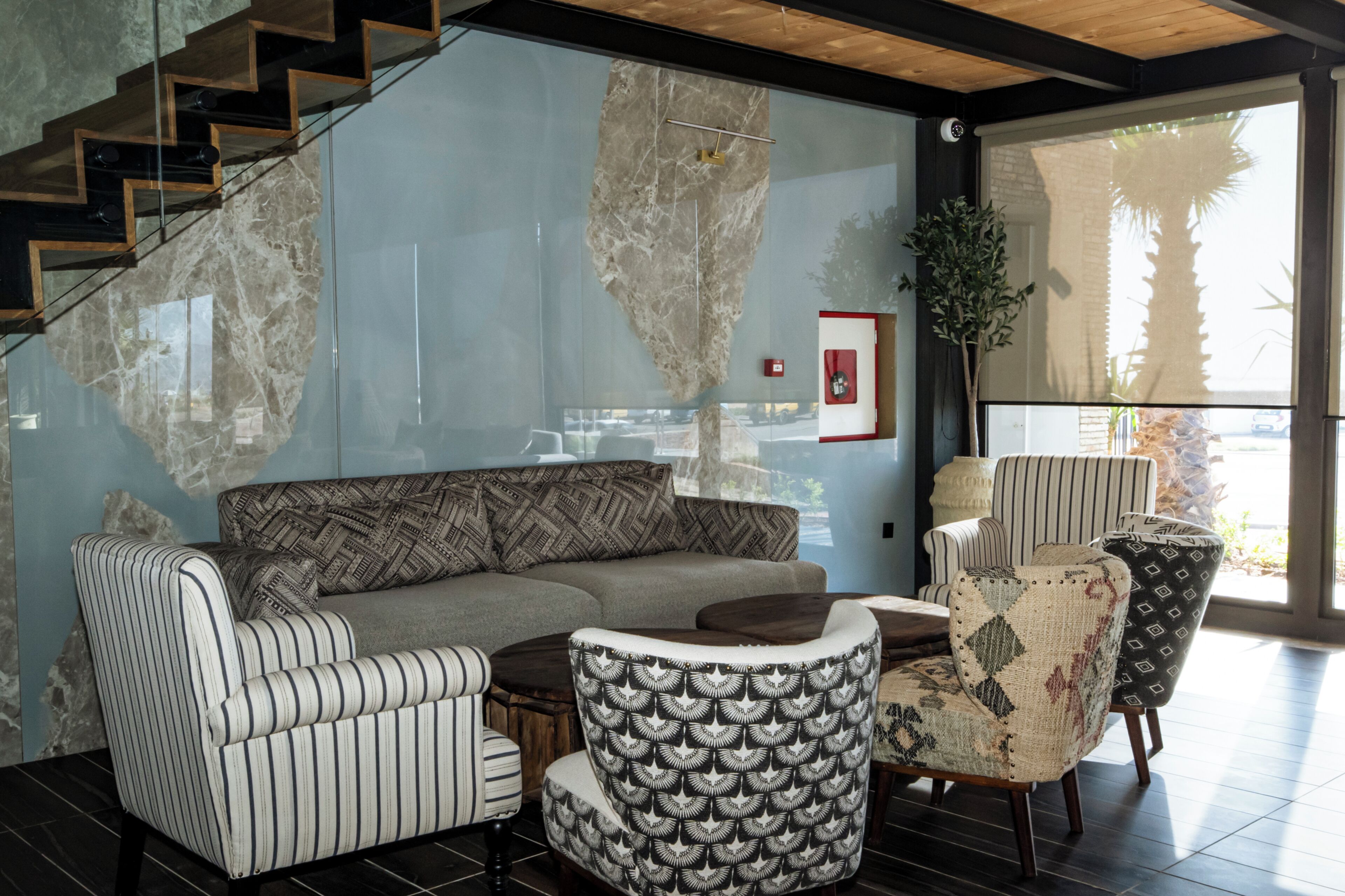 A modern living room with a sofa, striped armchairs, a patterned armchair, a coffee table, and a staircase.