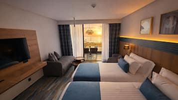 Une chambre d’hôtel avec deux lits, une télévision, un canapé, une petite table et une vue sur le coucher du soleil par la fenêtre.