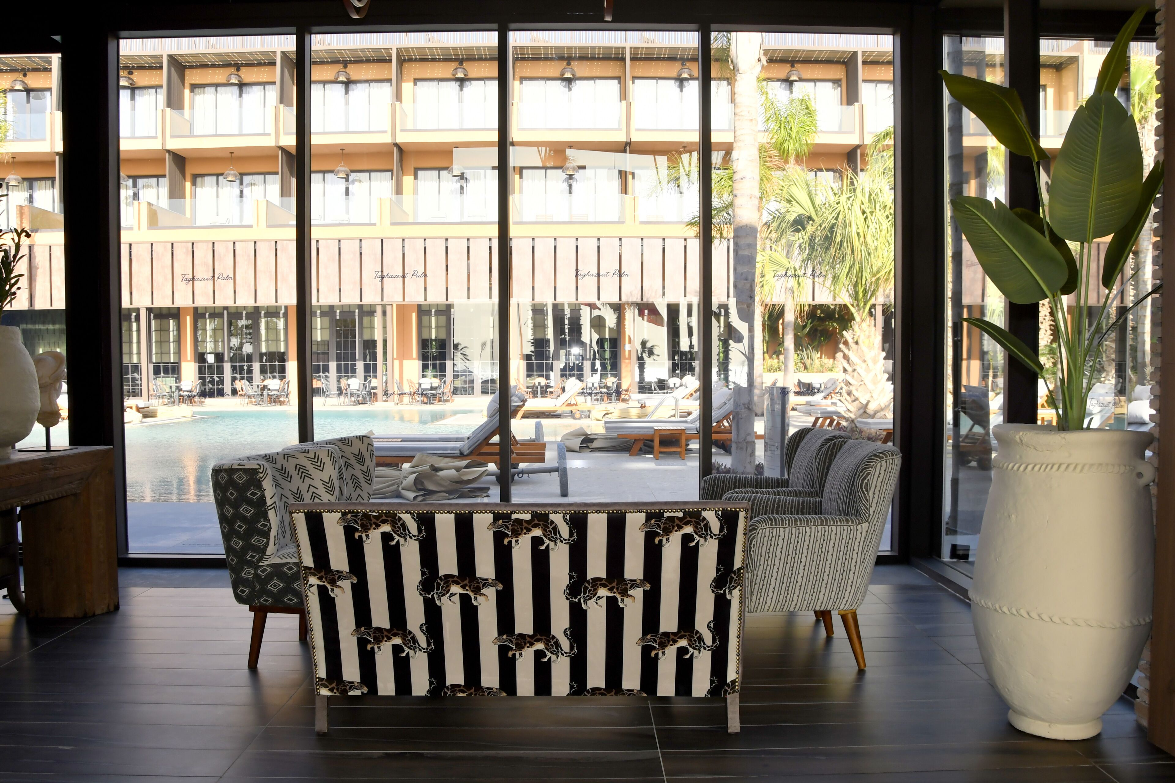 Un interior moderno con un sofá, ventanas amplias y vistas a una piscina y un edificio.