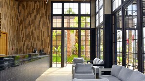 A reception area with a counter, seating area, and large windows. - Palm Taghazout Hotel (Tamraght)