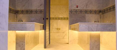 A bathroom with marble walls, a central sink, and a shower area.