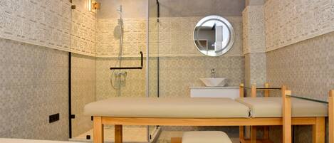 A modern bathroom with a glass shower enclosure, a round mirror, a sink, and a bench.