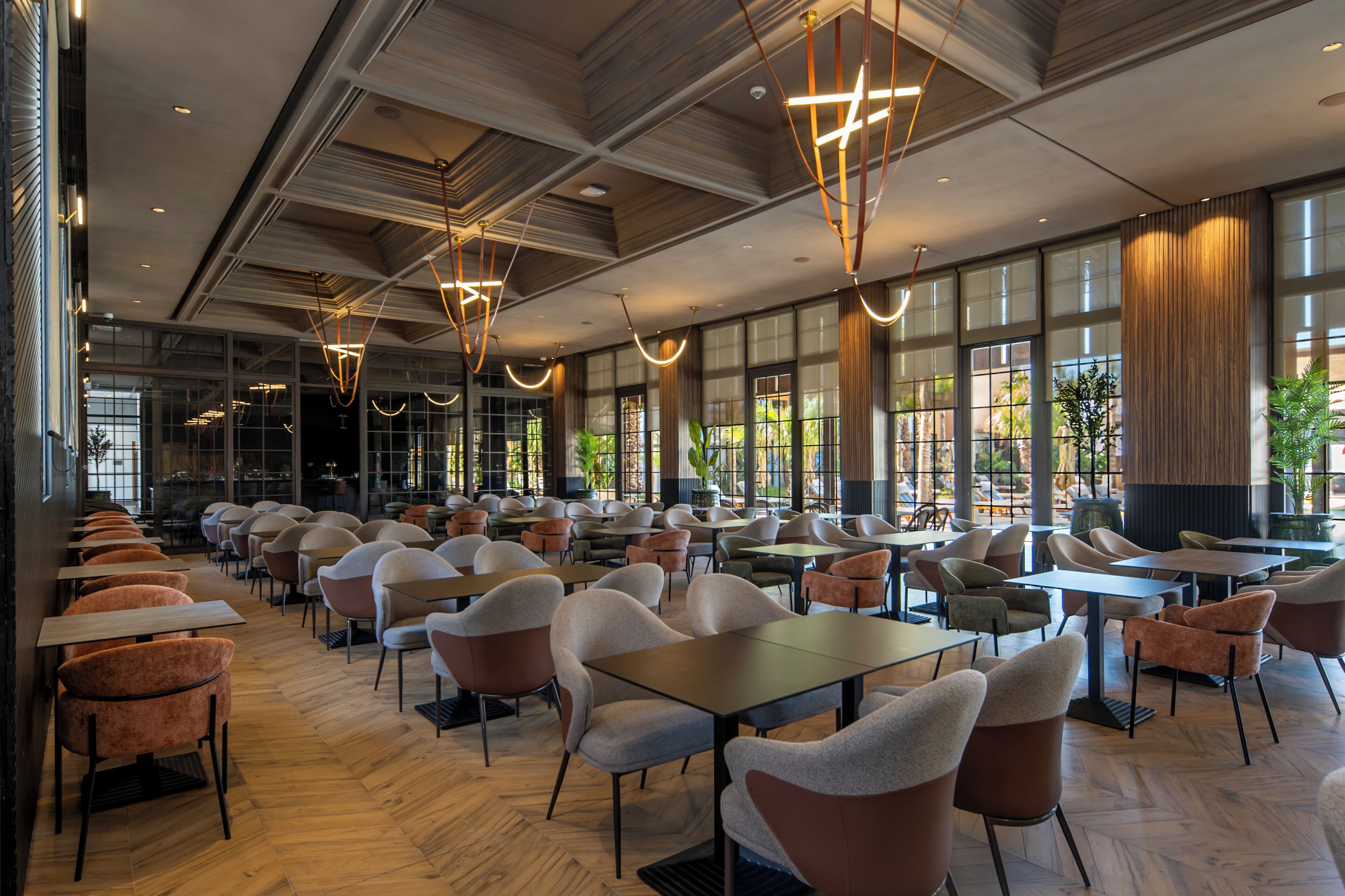 A spacious indoor dining area with multiple tables and chairs, large windows, and modern pendant lighting.