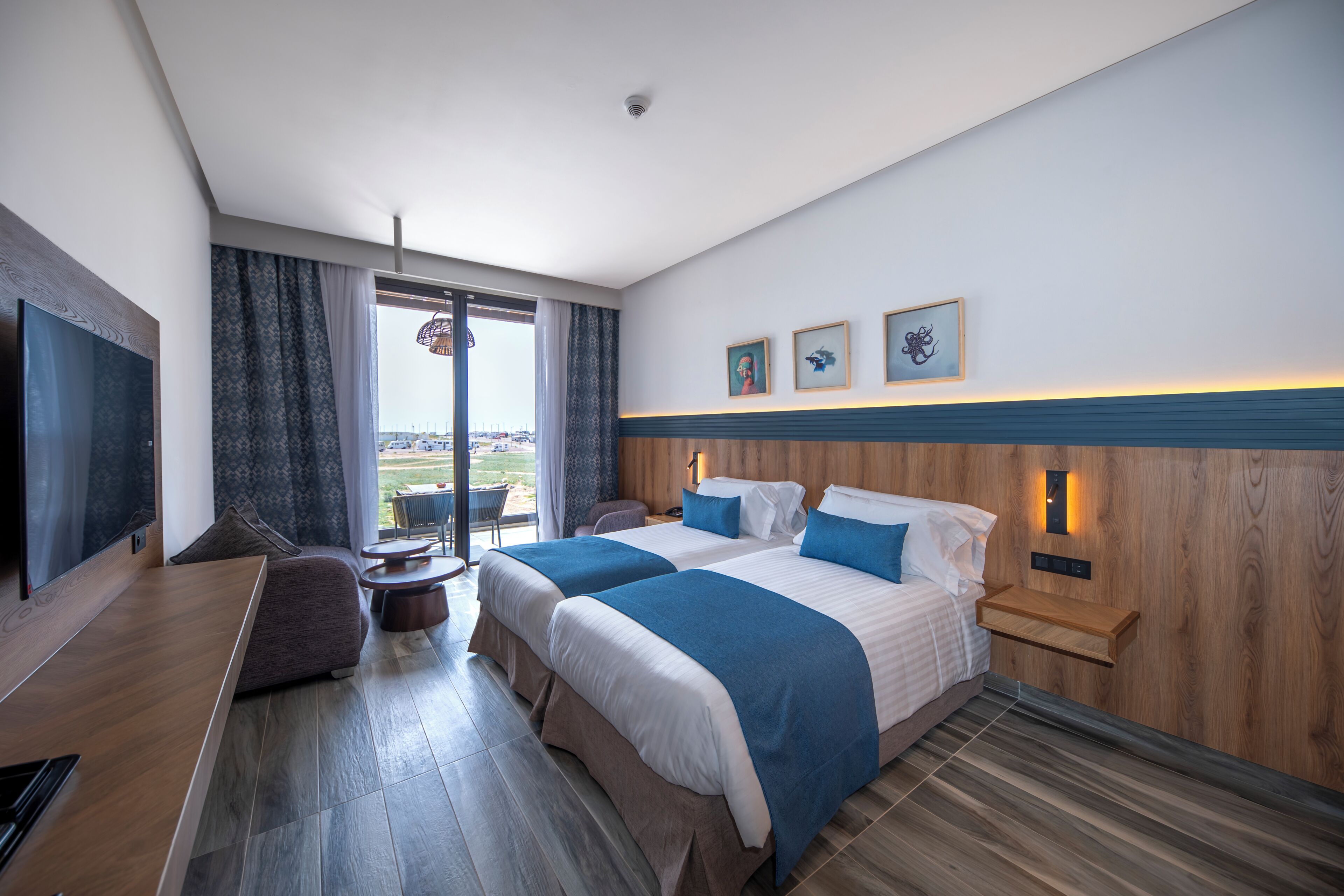 A modern hotel room with two beds, a TV, a balcony, and a city view.
