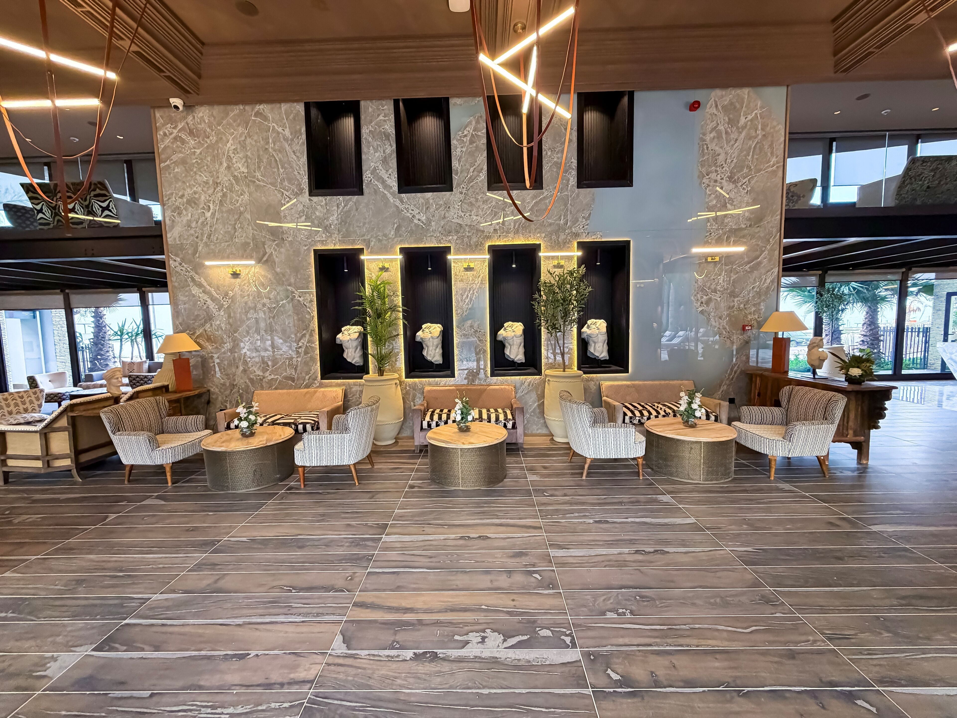 A spacious lobby with a marble wall, multiple seating areas, and large windows providing natural light.
