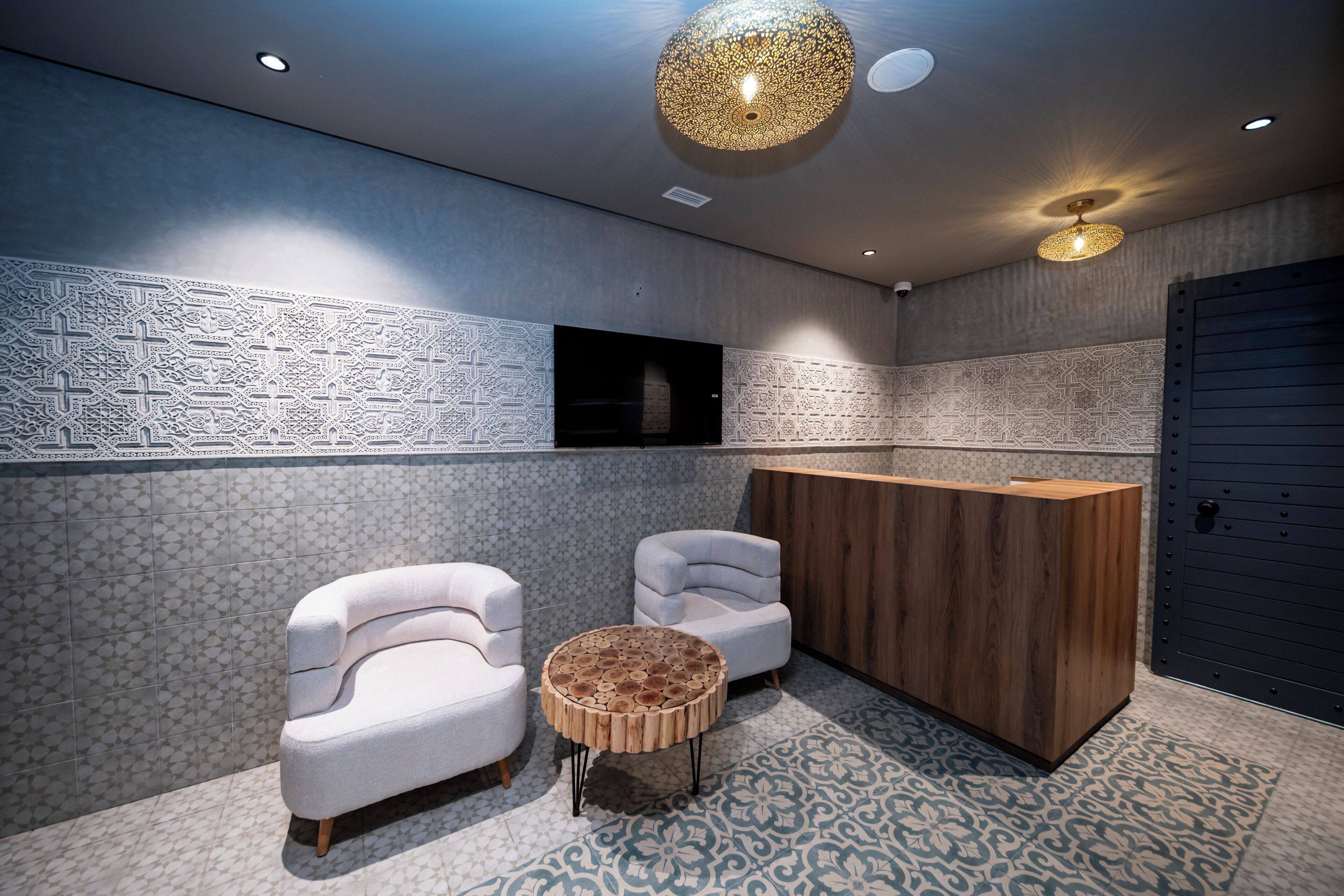 A modern reception area with patterned walls, two white armchairs, a wooden reception desk, and a unique round coffee table.