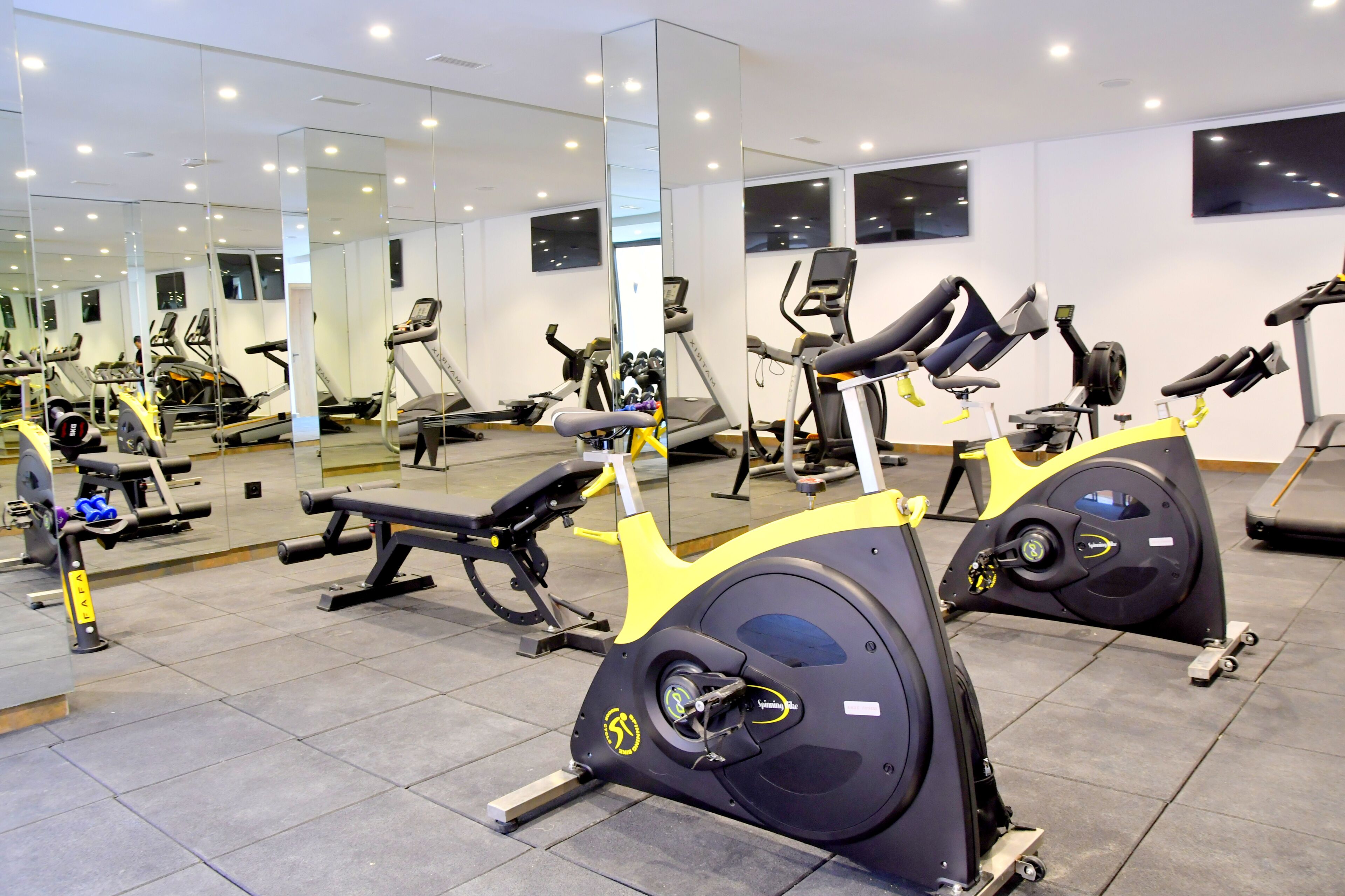 A gym with exercise equipment, mirrors, and a tiled floor.