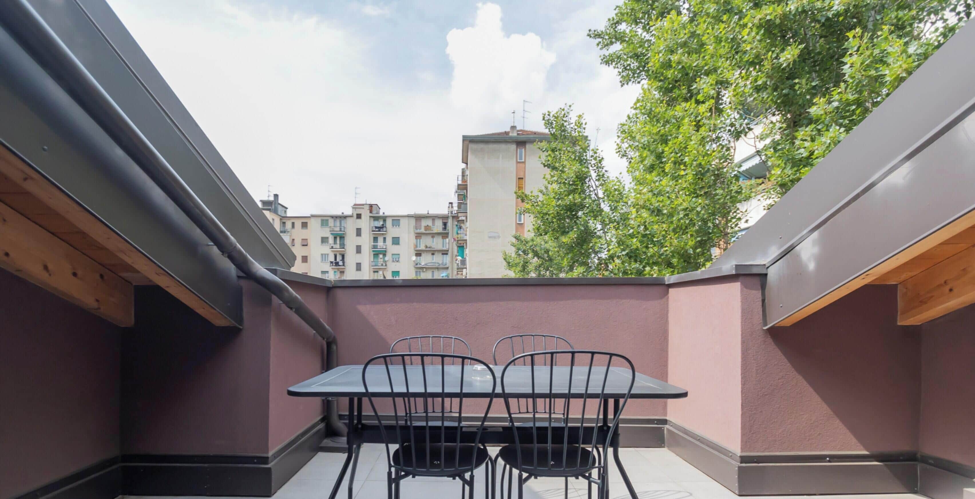 A balcony with a table and chairs, a view of buildings, and a tree.