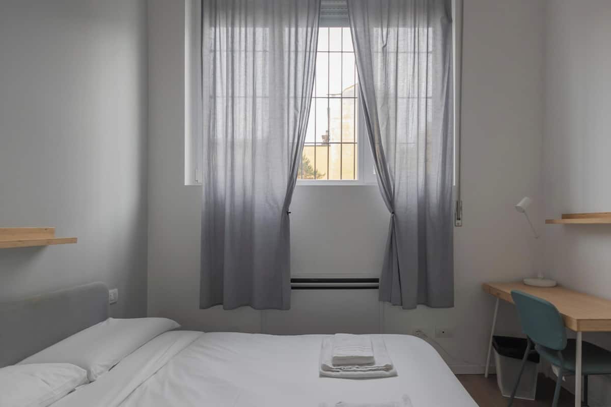 A bedroom with a bed, a desk, and a window with curtains.