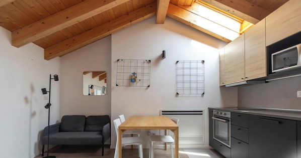 A compact kitchen with a wooden ceiling, a dining table with chairs, a sofa, and a built-in oven. - Hotiday Milano Frattini (Milan)