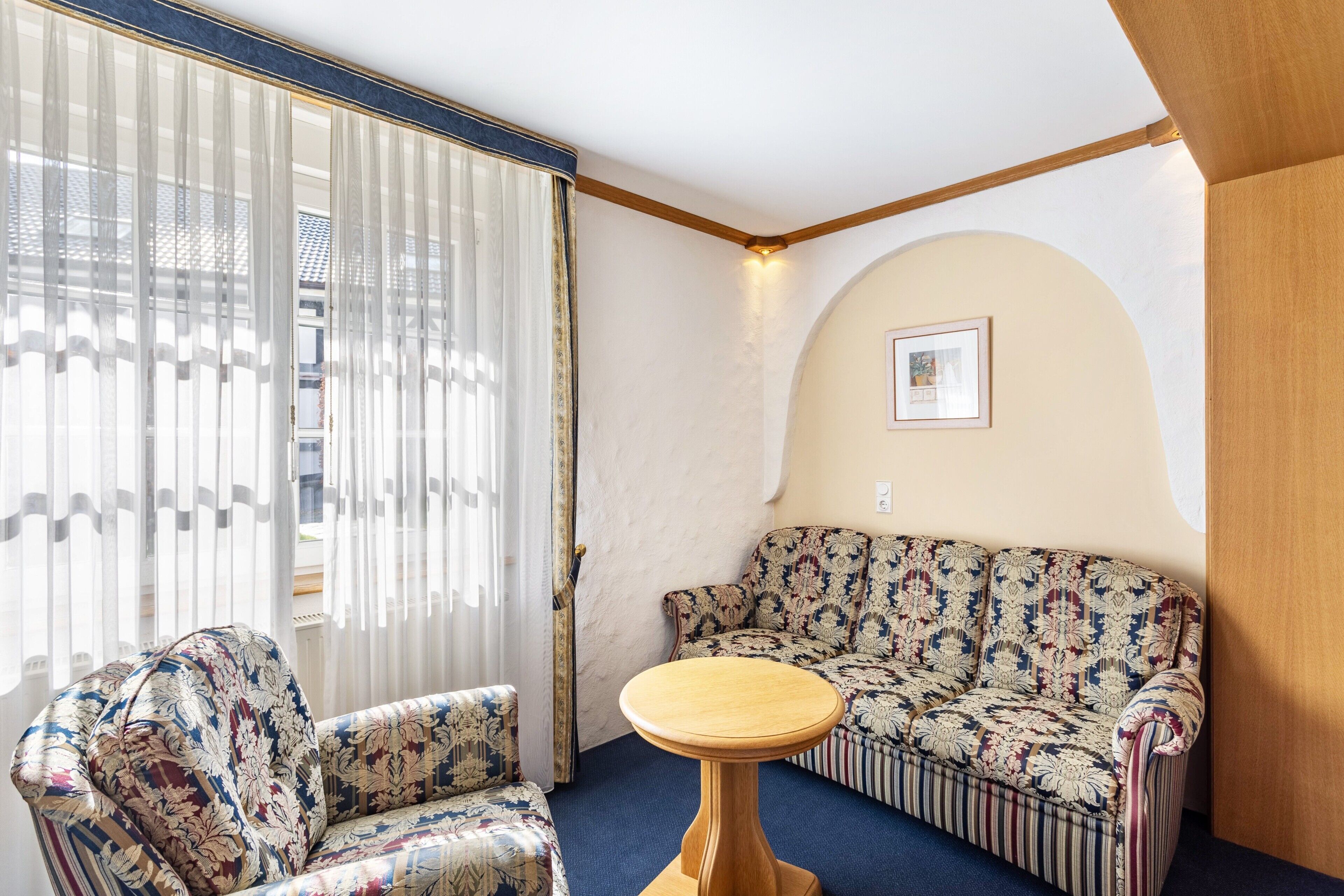 A room with a sofa, a chair, a round table, and a window with curtains.