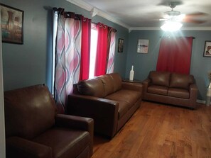 A living room with two brown leather sofas, a wooden floor, and a ceiling fan.