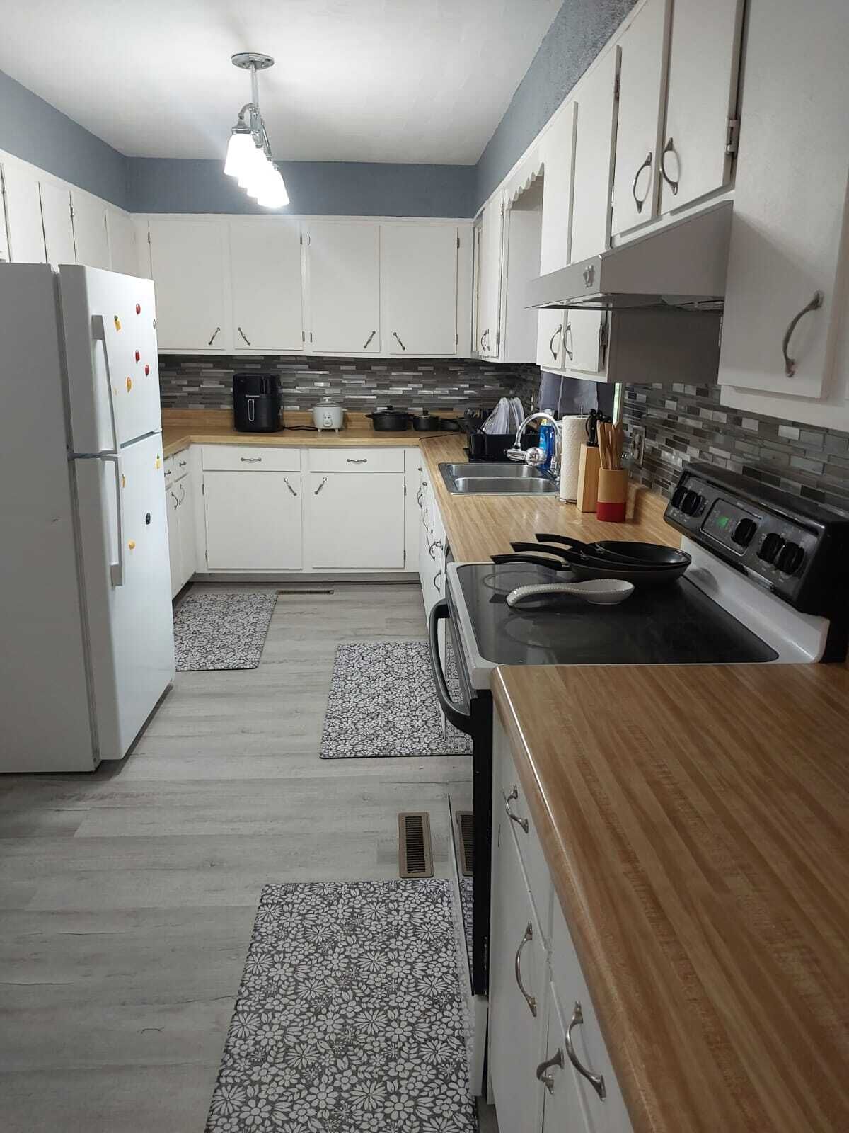 Une cuisine moderne avec des armoires blanches, un plan de travail en bois, une cuisinière et un réfrigérateur.