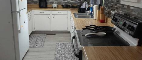 A modern kitchen with white cabinets, a wooden countertop, a stove, and a refrigerator.
