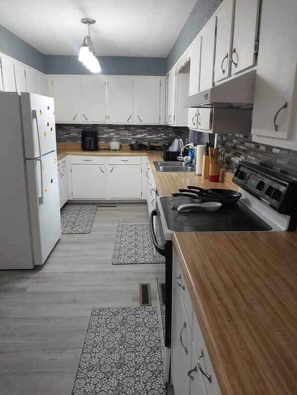 A modern kitchen with white cabinets, a wooden countertop, a stove, and a refrigerator.